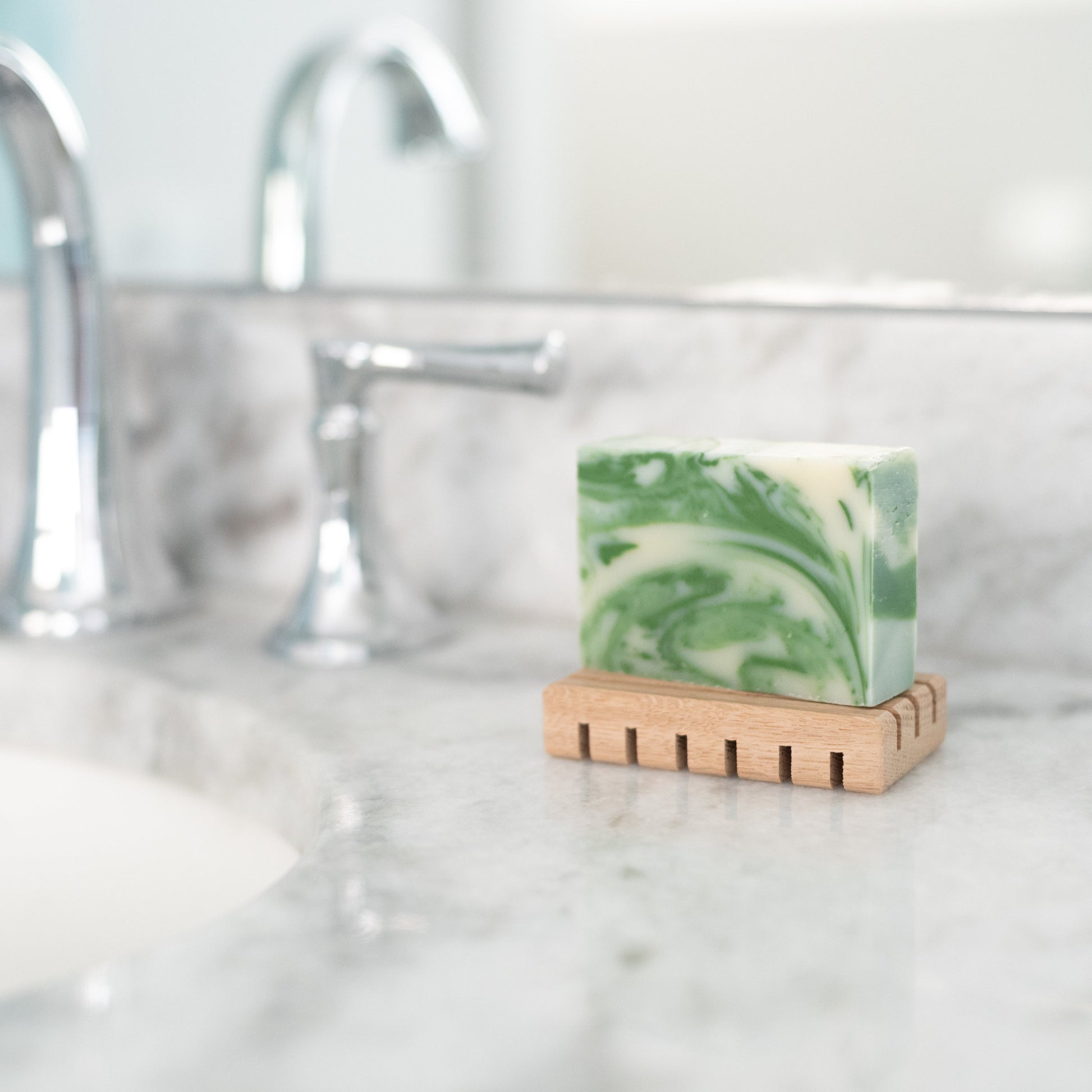 Bar of Christmas Wreath soap on a wood soap deck near the bathroom faucet on the counter