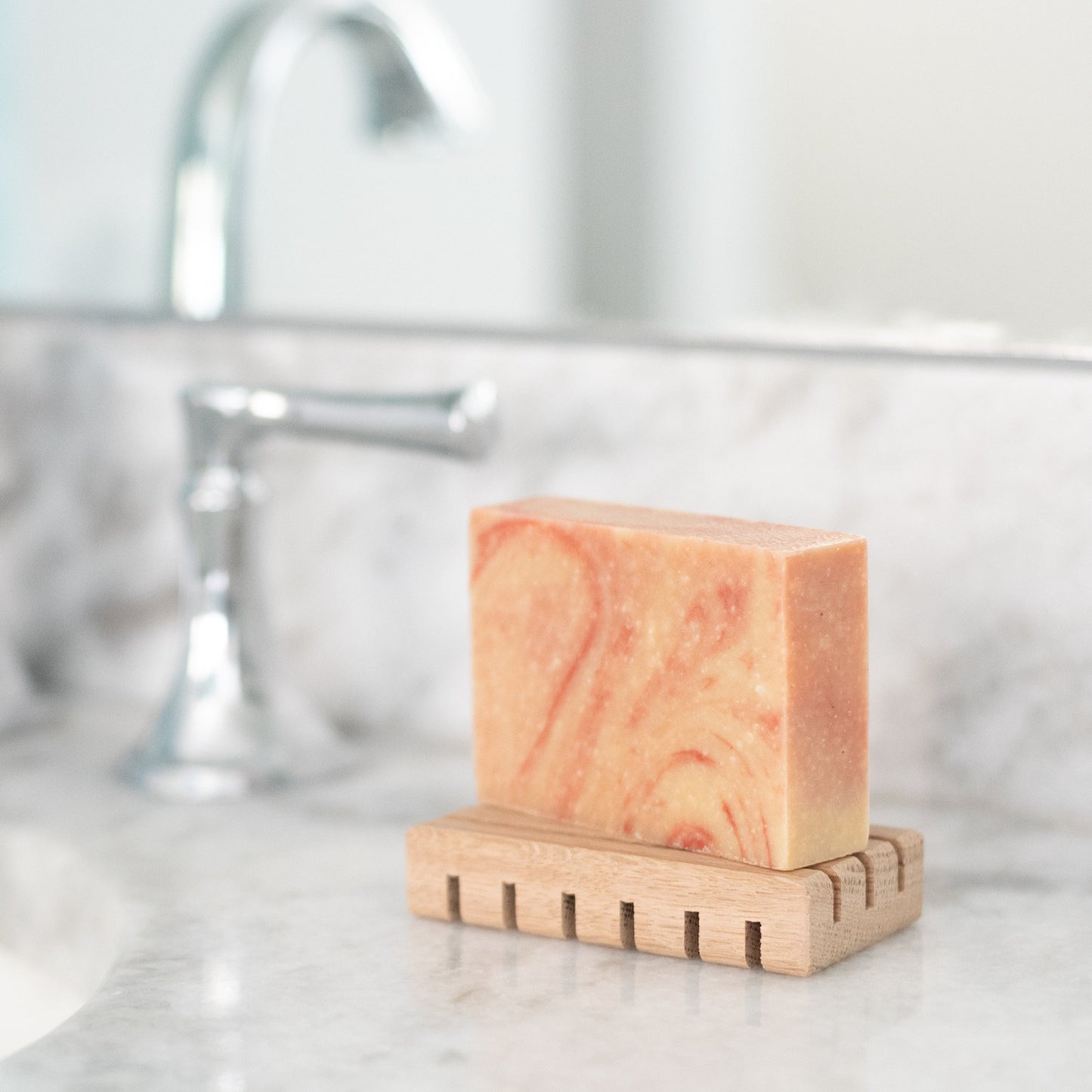peppermint swirl goat milk soap on wood deck next to faucet