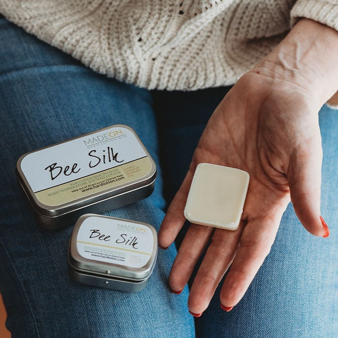 middle aged woman holding beesilk lotion bar in hand with lotion tins on lap