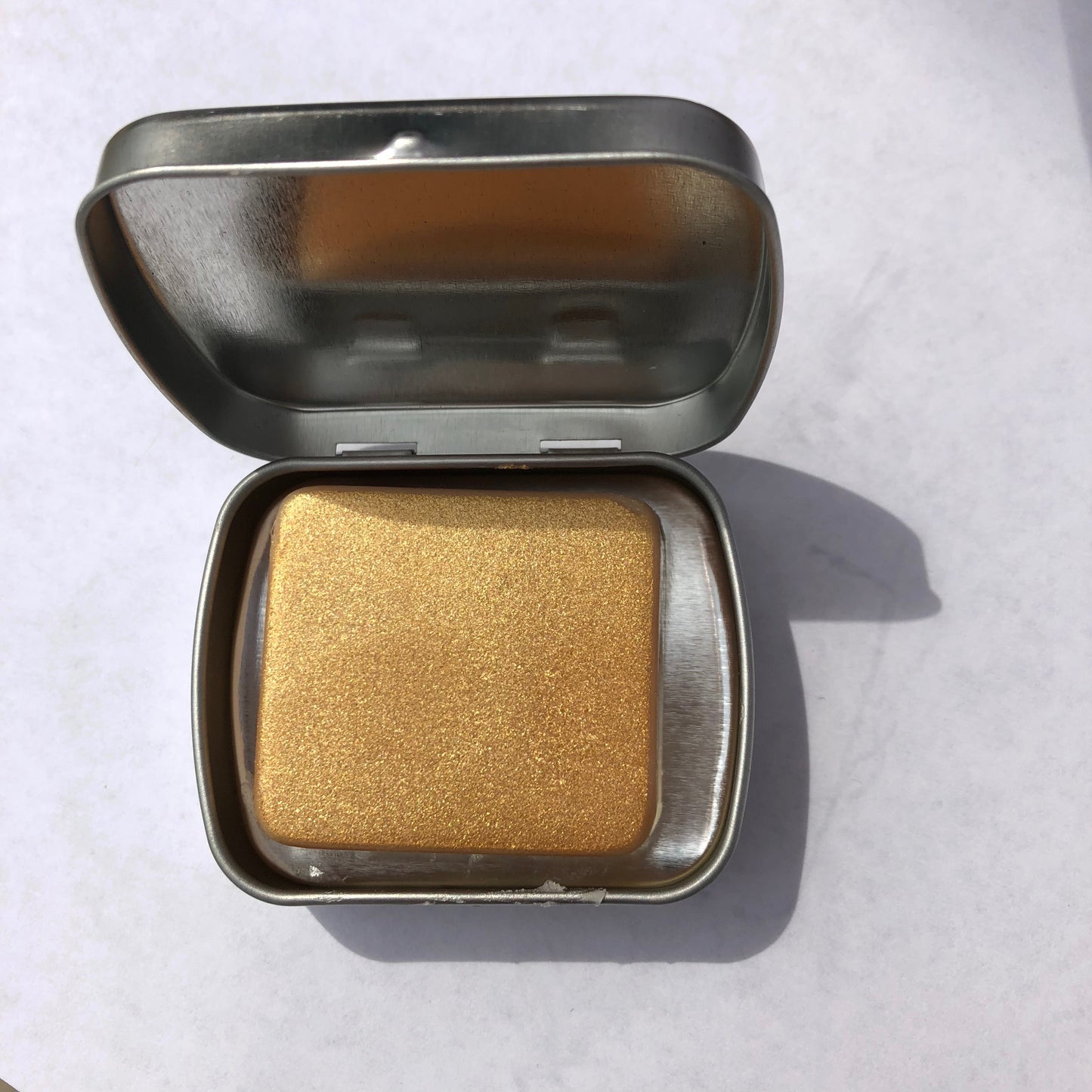 mica-glittered lotion bar for dry skin inside tin against white background