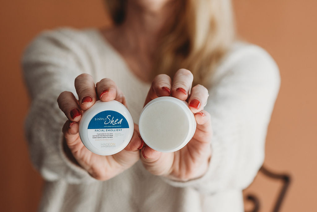 Woman holding up open container of 1 oz Simply Shea Facial Emollient