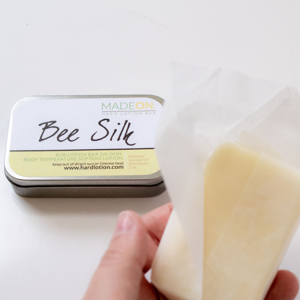 full size beeswax-based solid lotion bar in hand next to tin