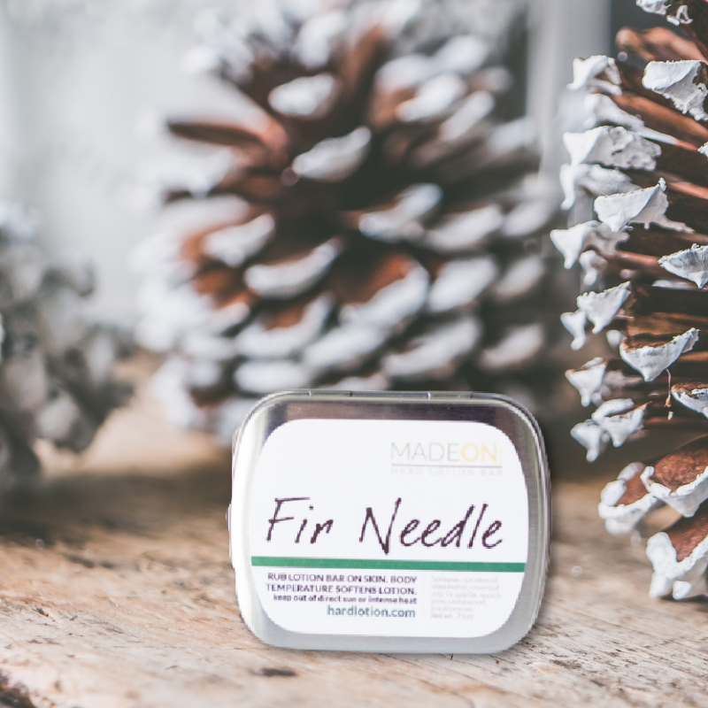 Pine-scented lotion bar in tin next to pine cones