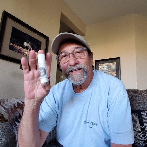 bearded middle aged man holding up a Foot Rub Lotion Stick in his home