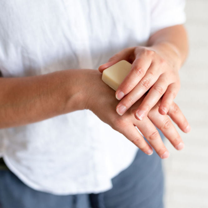 Hands applying Beesilk hard lotion bar to dry skin