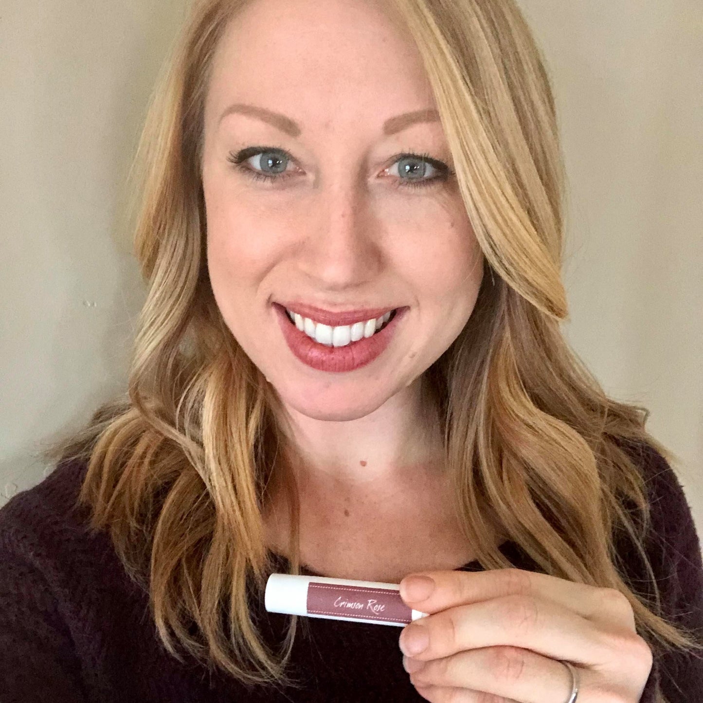 blonde woman holding tinted lip balm mineral lipstick in rose color