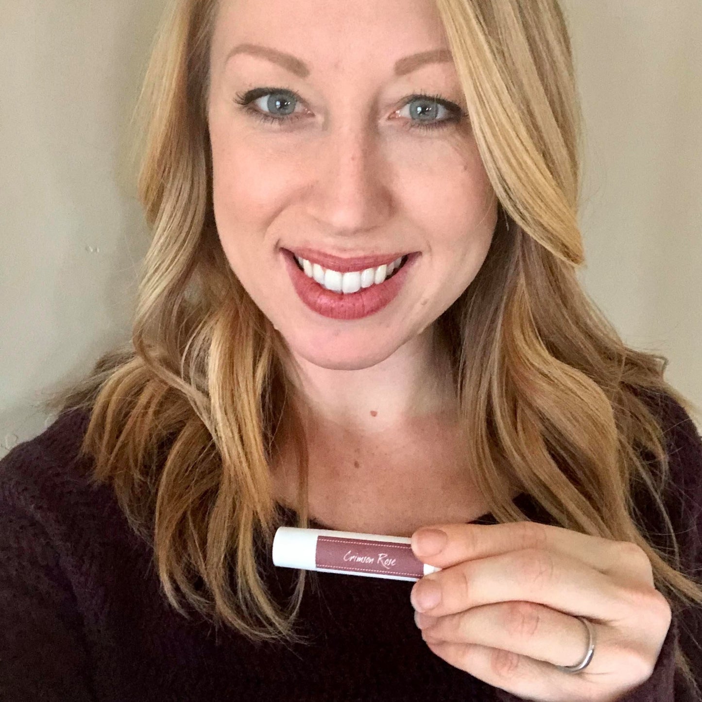 Woman holding Crimson Rose Tinted Lip Balm to show the color