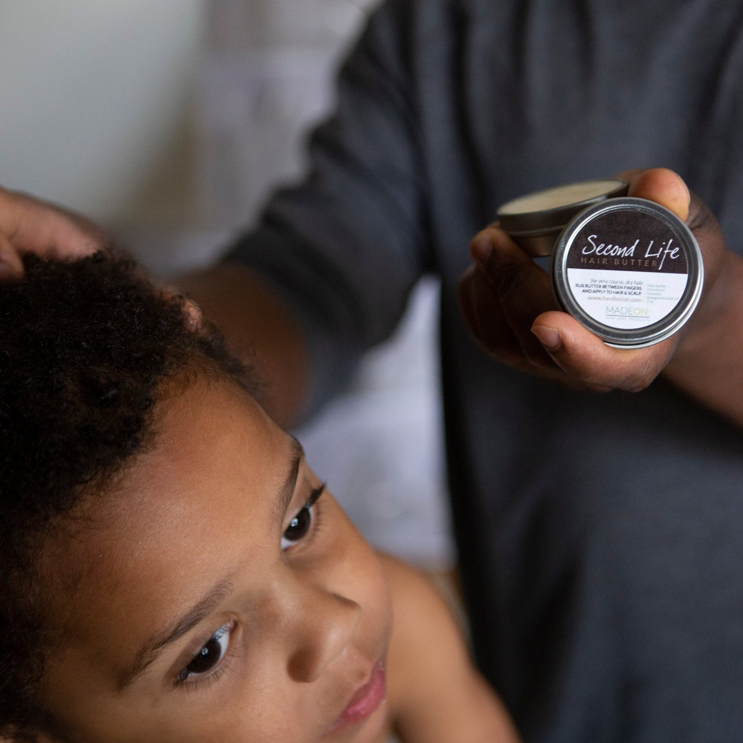 African American man applying Second Life Hair Butter to child's hair