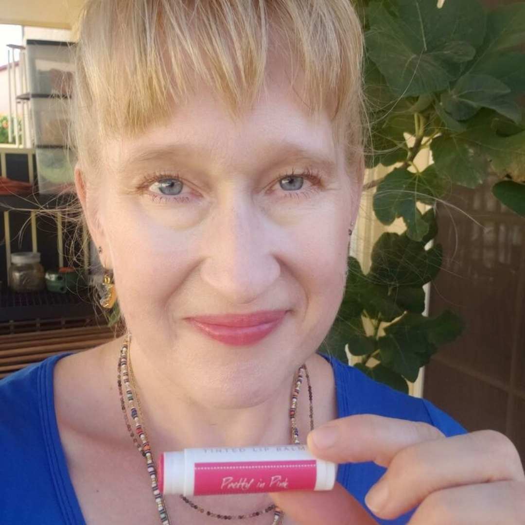 Femaie middle aged woman holding Pretty in Pink Tinted Lip Balm to show the color