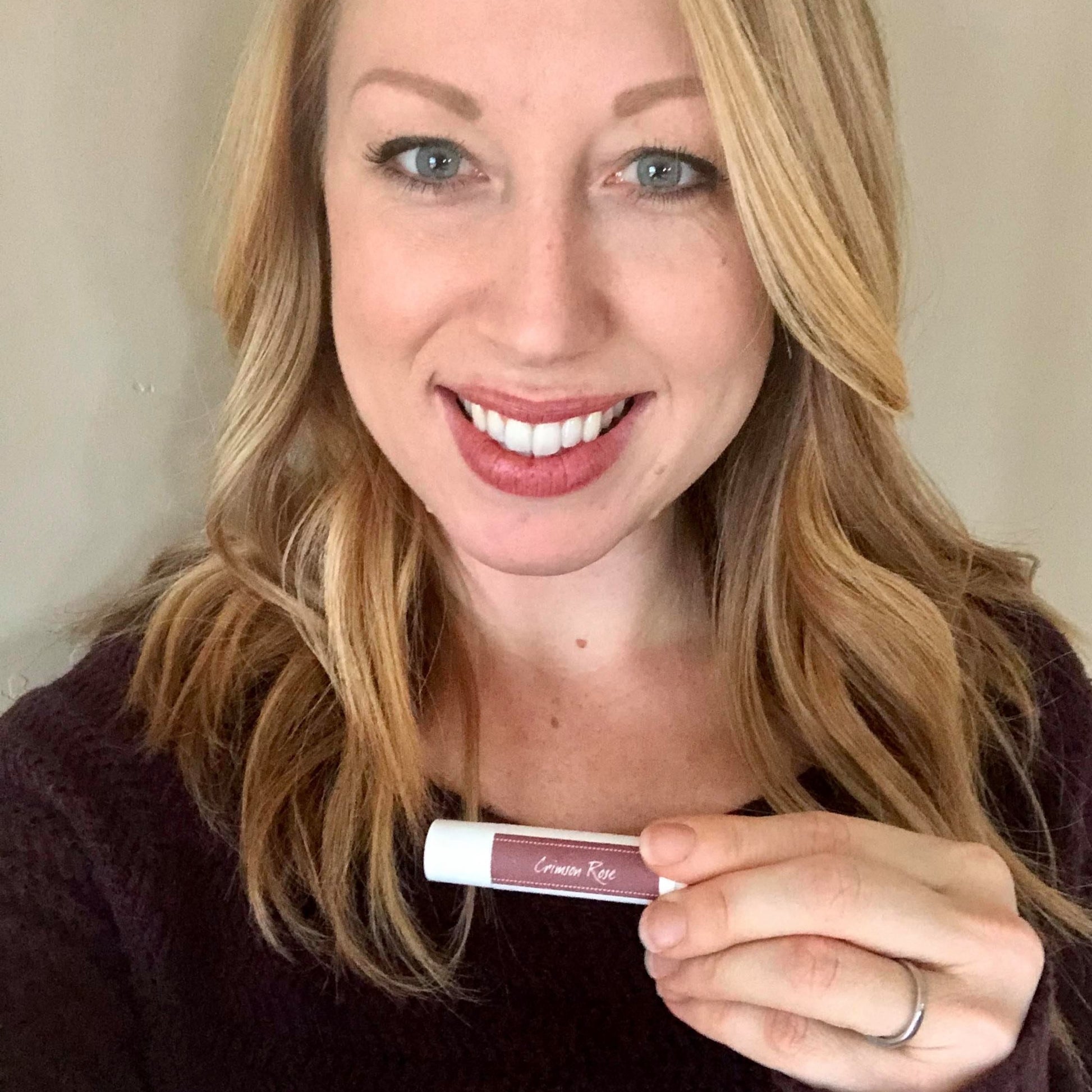 Woman holding Crimson Rose Tinted Lip Balm to show the color